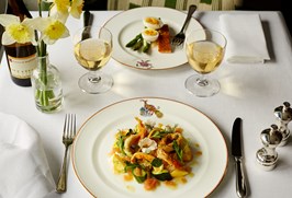 Two plates of food on a white linen table cloth with a bottle of white wine and two glasses