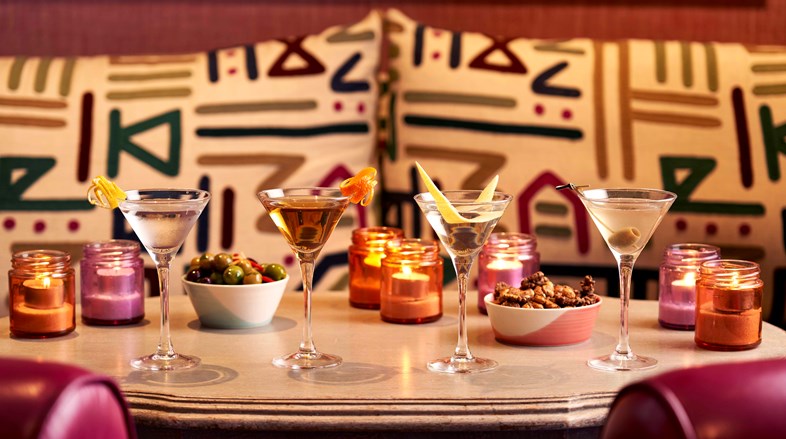 A variety of different Martini cocktails positioned on a table alongside bar snacks