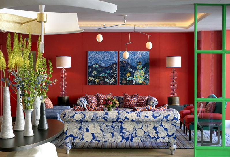 A view of the lobby reception area at 9-11 Richmond Buildings featuring two blue and white floral sofas behind a large central sculptural table and pendant light hanging above. The walls are upholstered in a red fabric with statement artwork hung in front.
