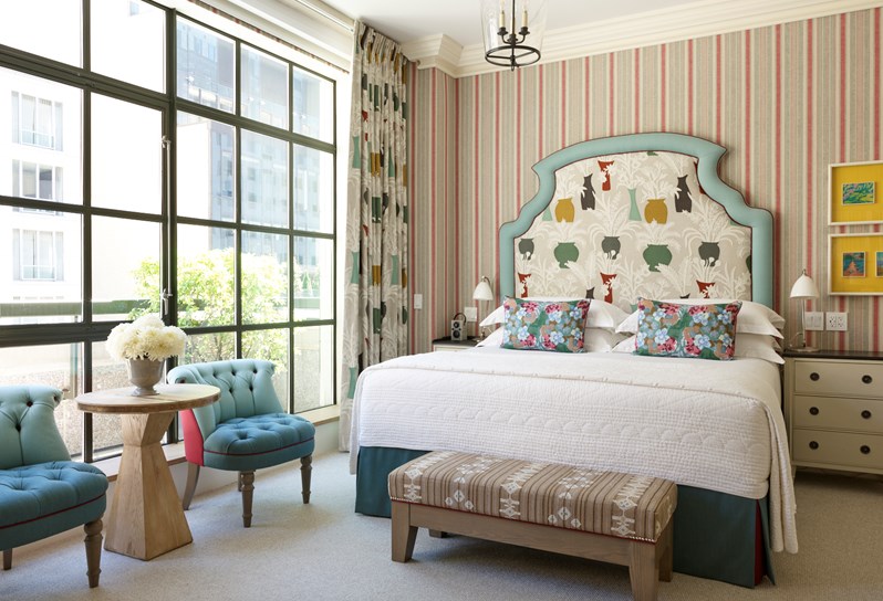A bedroom with a bed that has an upholstered headboard and windows dressed with a matching contemporary fabric design