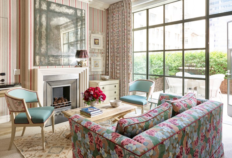 A drawing room of a one bedroom suite which includes a sofa, two chairs and coffee table. There is an open loft style door that leads to an outdoor terrace.