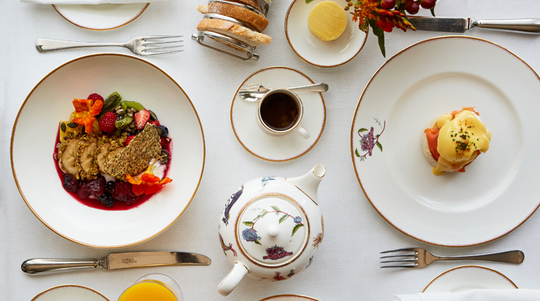 A selection of breakfast dishes including a superfood breakfast bowl and eggs Royale are placed on a table dressed with a white table cloth