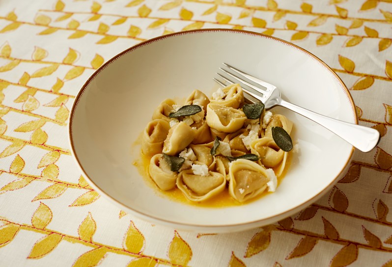 Squash tortellini with sage and smoked ricotta served in a bowl on Kit Kemp's tea leaf fabric in the yellow colourway