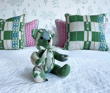 This Willow "Chubby check " bear is a new and limited edition member of Kit's patchwork Toy collection. Made from Kit's "Chubby Check " Woven Cotton fabric, in Green Blue and Ecru, inspired by a blanket, it's a natural place is on any bed.
Photographed on a bed, on a white bed spread with pink, and green cushions in back ground