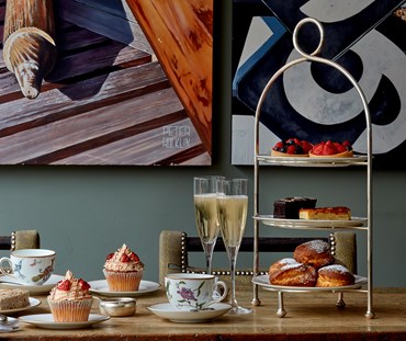 silver 3 plate cake stand, with mythical creatures 3 ,20.5 cm plates on it, displayed on a table dressed for a champagne tea, with mythical creature teacup and saucer.