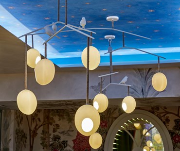 Our bright blue starry night wallpaper, featuring scattered yellow stars, outlined lined with wine coloured shadows , photographed in situ as a ceiling wallpaper, with a large rocking robin bird chandelier in the foreground