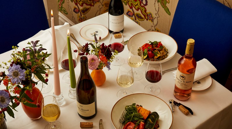 A table laid for a wine dinner at Covent Garden Hotel. Two plates of food are paired with a number of different wines and the table is decorated with flowers and candles in oranges, purple, pink and green.