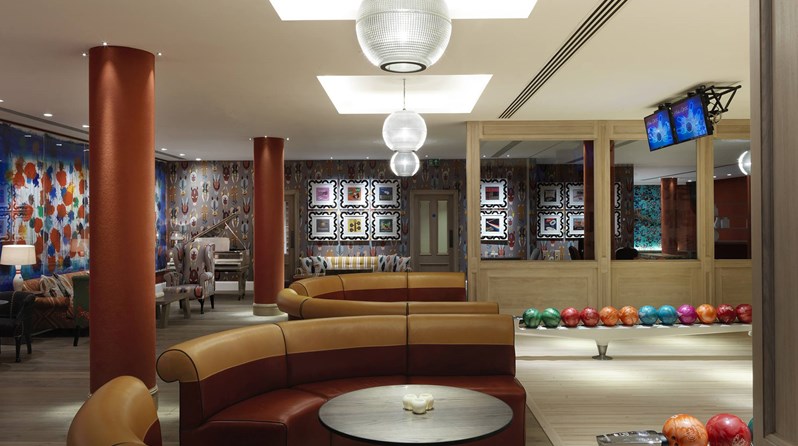 Lounge area with comfortable leather sofas in red and yellow in half circles facing the original 1950's bowling alley with its brightly colored bowling balls.