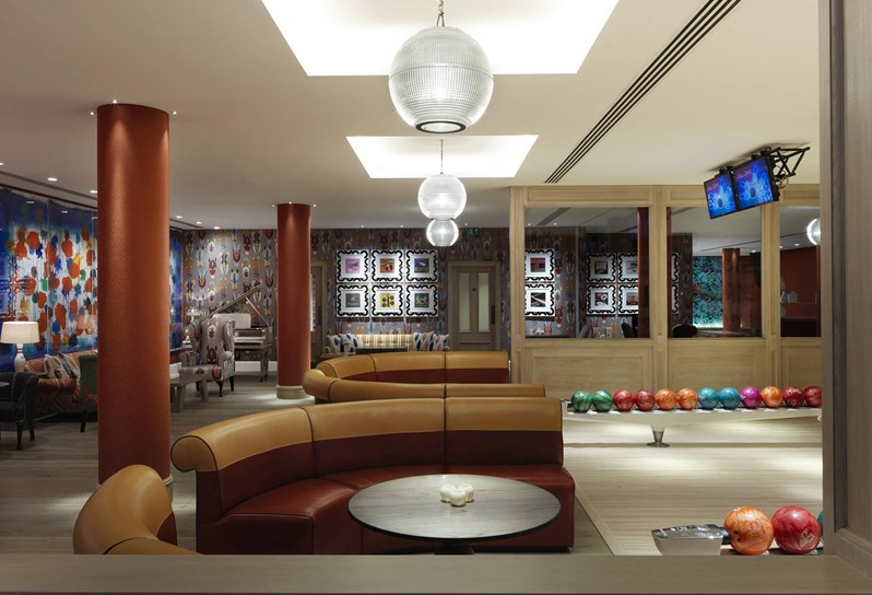 Lounge area with comfortable leather sofas in red and yellow in half circles facing the original 1950's bowling alley with its brightly colored bowling balls.