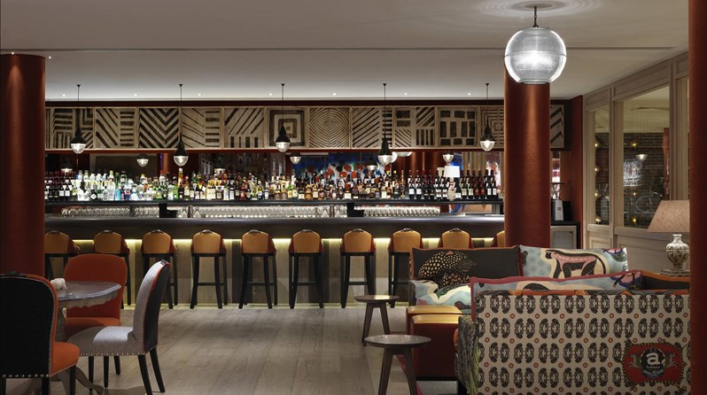 A fully stocked bar next to the bowling alley, complete with ample colorful seating in both lounge style comfortable furniture as well as high chairs in front of the bar.