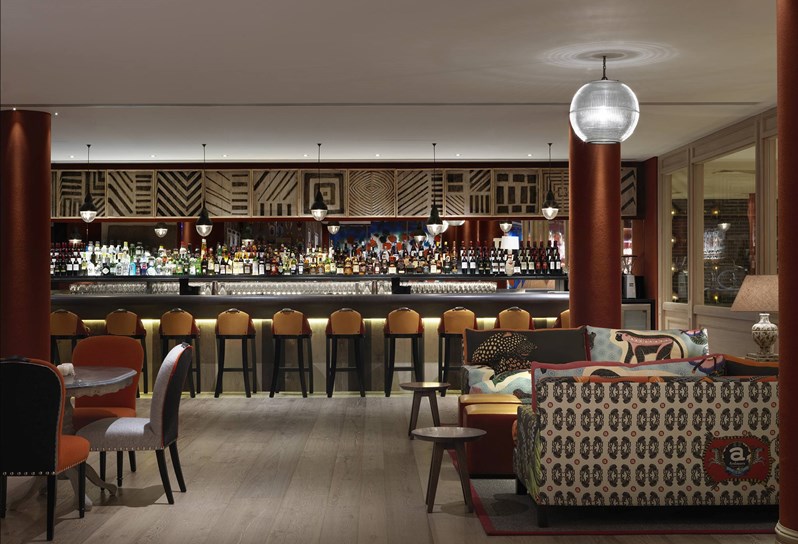 A fully stocked bar next to the bowling alley, complete with ample colorful seating in both lounge style comfortable furniture as well as high chairs in front of the bar.