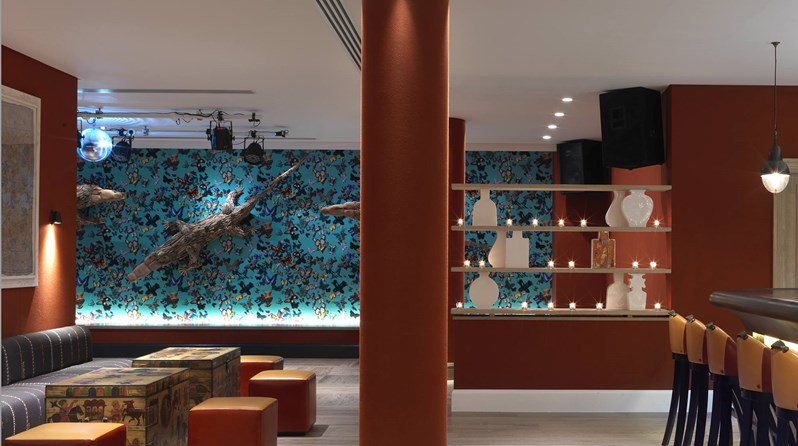 View from the ample seating in the bar in toward a dance floor with large crocodile sculptures climbing on a multiple colored wall with butterflies.