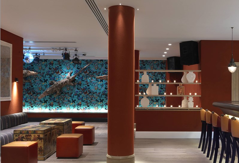 View from the ample seating in the bar in toward a dance floor with large crocodile sculptures climbing on a multiple colored wall with butterflies.