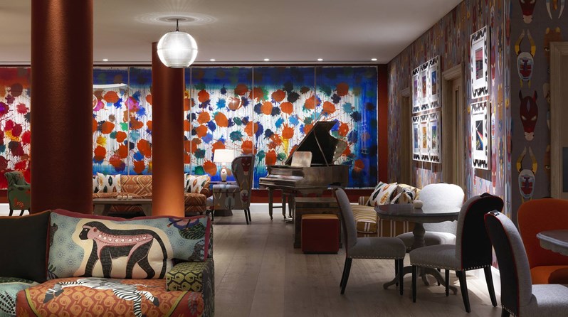 A brightly colored wall in the back with a grand piano in front, surrounded by several seating areas in sofas and armchairs.