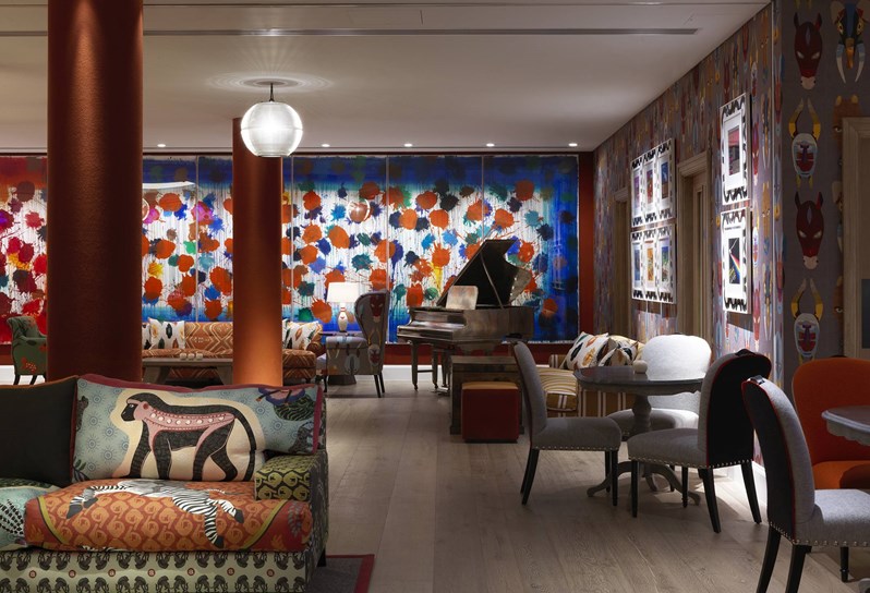 A brightly colored wall in the back with a grand piano in front, surrounded by several seating areas in sofas and armchairs.