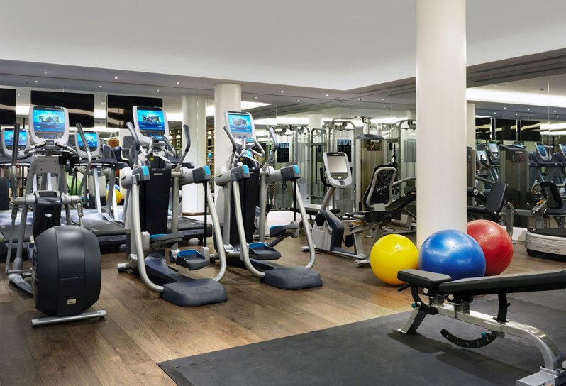 A fully equipped gym with floor to ceiling windows, containing step machines, treadmills, rowing machine and Pilates balls.