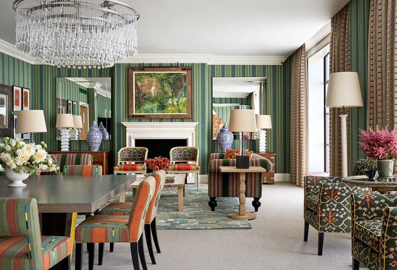 Shot of the living room in a One Bedroom Suite at the Crosby Street Hotel dinner table on the left and at the back a fire place and two chairs in front, a coffee table and on the side two sofas and lamps on tables all around the room