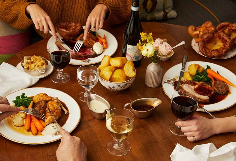 Three plates of roast dinner on a table with red wine and wine glasses