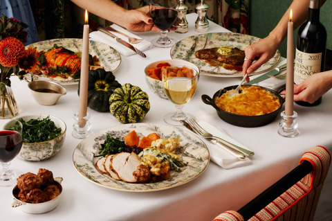 This image is to promote Brasserie Max's Thanksgiving menu at Covent Garden Hotel. It shows a seasonal autumn dining table featuring a traditional roast dinner with turkey, stuffing and seasonal vegetables, alongside steak, roasted squash, greens and a baked side dish, served on Tall Trees crockery with wine, candles and autumnal flowers.