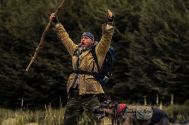 A film still from Hear of the Beast, in this image we can see Brad Pitt celebrating and cheering as his dog stands by him.