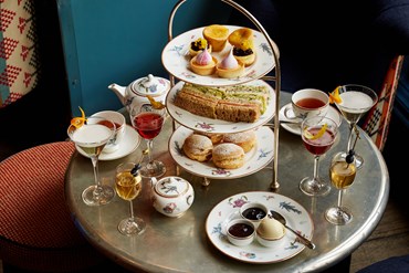 Afternoon tea displayed on a table in Oscar restaurant at the Charlotte Street Hotel. The fine bone china is Mythical Creatures by Kit Kemp for Wedgwood along side a 3 tier cake stand, sandwiches and scones.