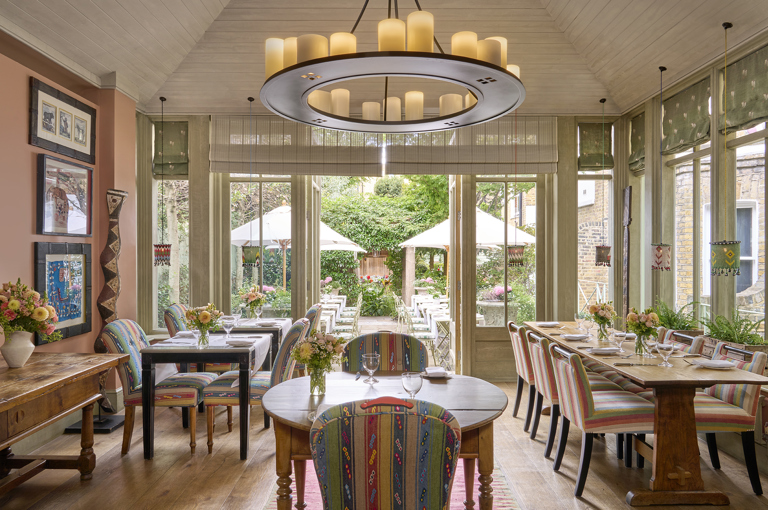 A wide view across The Orangery restaurant at Number Sixteen hotel, looking through to the garden beyond. The restaurant tables are laid with crockery, cutlery and glassware.