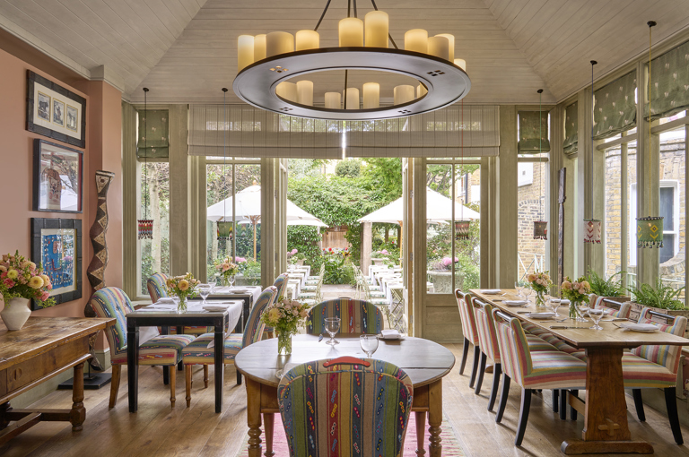 A wide view across The Orangery restaurant at Number Sixteen hotel, looking through to the garden beyond. The restaurant tables are laid with crockery, cutlery and glassware.