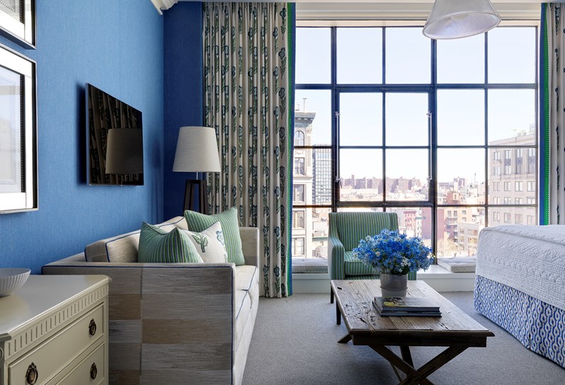A spacious bedroom in this beautiful junior suite with high ceilings, floor to ceiling windows and views over SoHo. A beautiful colour scheme with bright blue walls and a cream sofa.