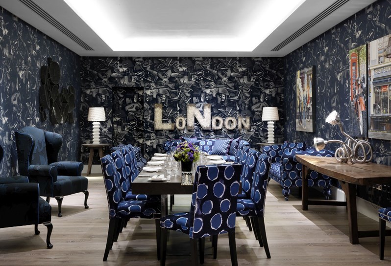 The Archer Room in blue tones with original John Paul Gaultier wallpaper, two comfortable armchairs and quirky design pieces surrounding a rectangular table set for private dining for 10 people on comfortable chairs matching the rest of the decor.