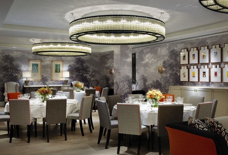 Three large round tables set for private dining with comfortable chairs, with three intricate circular chandeliers hung from the ceiling and interesting artwork on the nature inspired dusk colored walls.