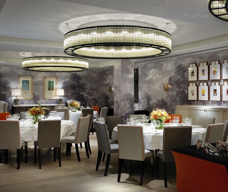 Three large round tables set for private dining with comfortable chairs, with three intricate circular chandeliers hung from the ceiling and interesting artwork on the nature inspired dusk colored walls.