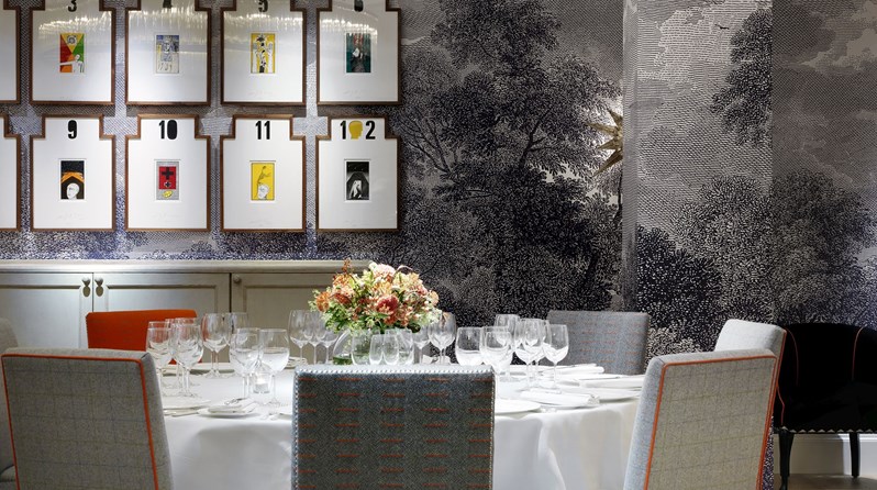 A closeup of a round table with chairs, beautifully set for private dining in a private event space, complete with a fresh flower arrangement on the table and original artwork on the wall.