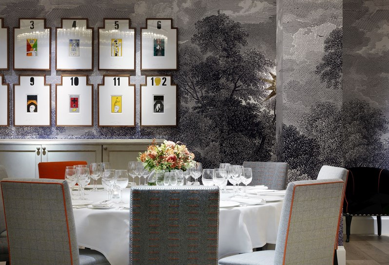 A closeup of a round table with chairs, beautifully set for private dining in a private event space, complete with a fresh flower arrangement on the table and original artwork on the wall.