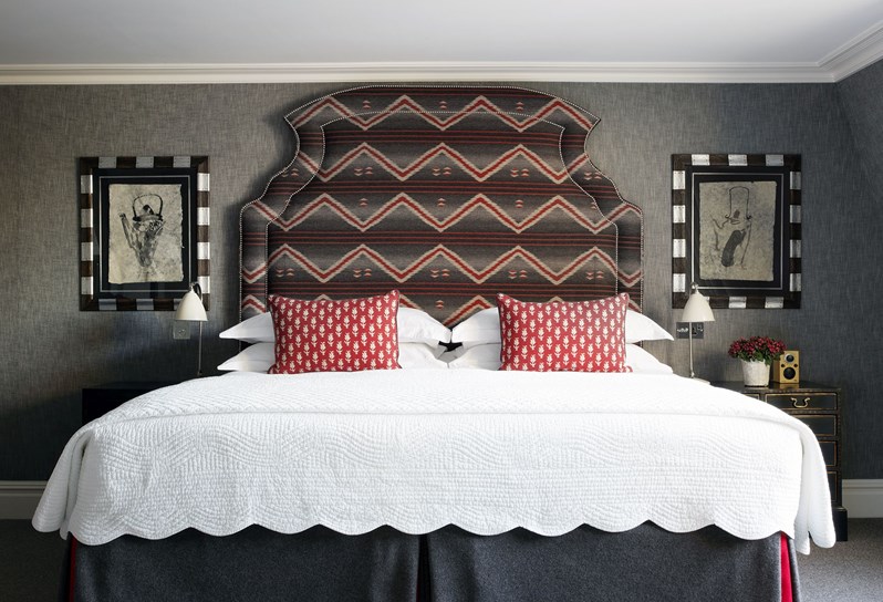 A bedroom with large king size bed, red cushions and a dark patterned headboard. There is a frame either side of the bed hanging above bedside tables.
