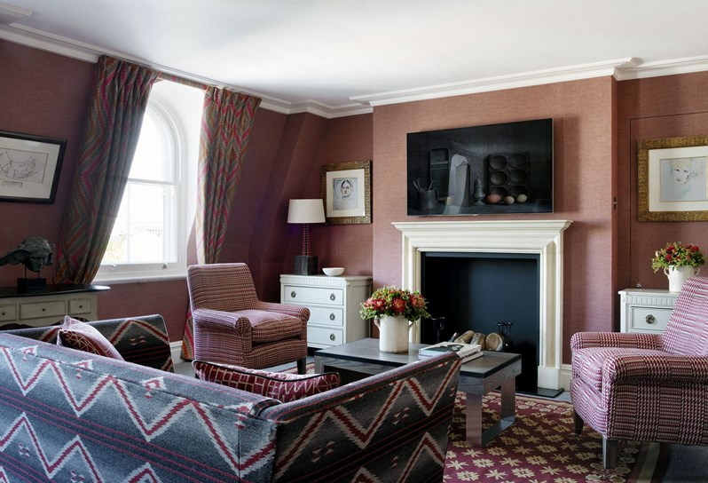 A lounge area onlooking a fireplace which has a TV above. There are 2 armchairs and a large sofa surrounding a coffee table in front of the fireplace.