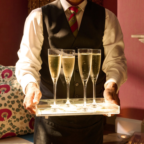 A waiter holding a tray filled with Champagne flutes in the Drawing Room at Crosby Street Hotel 