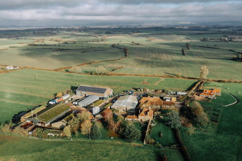 A far out shot of green landscape showing a farm and houses