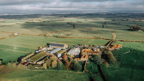 A far out shot of green landscape showing a farm and houses 