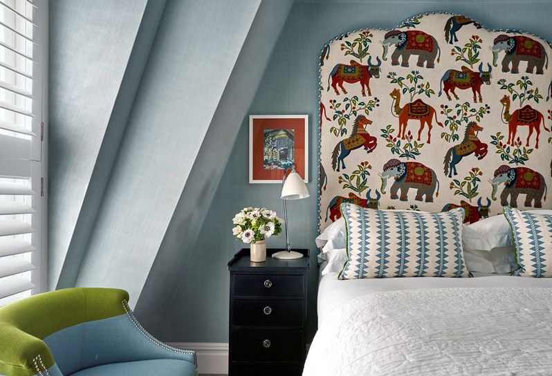 Front bedroom shot the bed in a superior room with plain light blue walls, colourful animal drawings on the headboard and a blue and green chair.