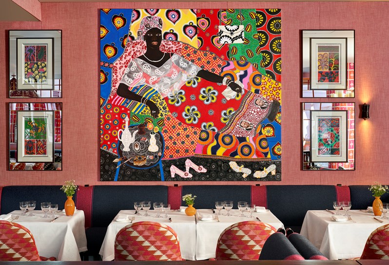 Four of the tables in the restaurant, beautifully set up with comfortable chairs on one side and a cushioned wall bench on the other, perfectly accompanied by original artwork on the walls.