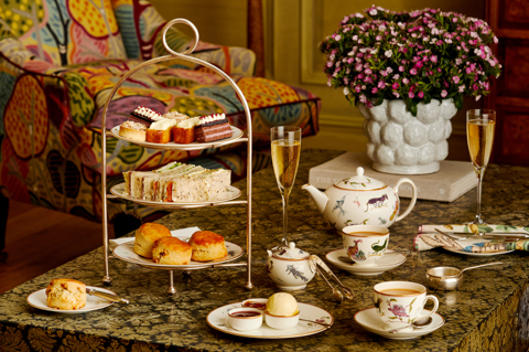 An Afternoon Tea at Oscar Restaurant set up on a low coffee table in the Drawing Room at Charlotte Street Hotel. On the table is a three-tiered cake stand, a teapot with two cups of tea and a sugar pot, two glasses of sparkling wine and plates with scones and accompaniments