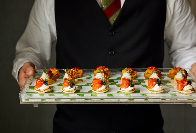 A waiter holding a tray of festive canapes, including mini cream cheese, smoked salmon and caviar pancakes,