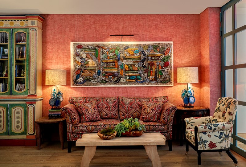 The Drawing Room at Warren Street Hotel with a sofa upholstered in a dark red patterned fabric and a small armchair in a cream, blue and red fabric. On the right hand side there is a painted cabinet filled with books