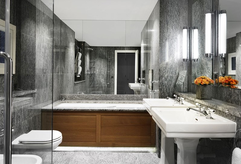 A granite bathroom containing a deep bathtub, a separate walk in shower, double basins, a bidet and a toilet.