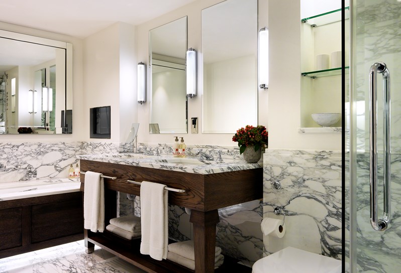 A white bathroom with grey and white marble. There is a double sink with mirrors above along the wall. There is a separate bath and shower.