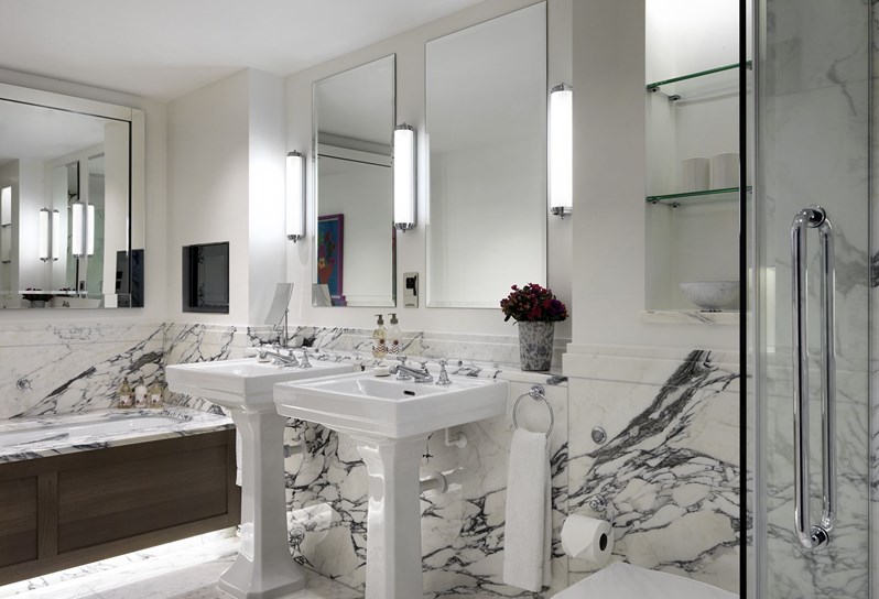 A white bathroom with grey and white marble. There is a double sink with mirrors above along the wall. There is a separate bath and shower.