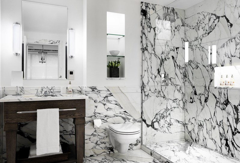 A white bathroom with grey and white marble. There is a single sink with a mirror above and a walk in shower along the length of the right hand wall.