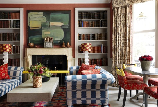 Two sofas placed opposite each other with a low coffee table between, arranged in front of a fireplace which has book cases on both sides. On the right there is also a dining table and chairs in front of large windows.