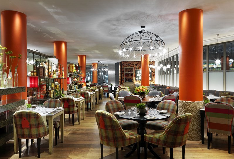 The ReFuel restaurant with round tables and upholstered chairs. The colorings are burnt orange and green. There's a large wrought iron chandelier in the middle of the room