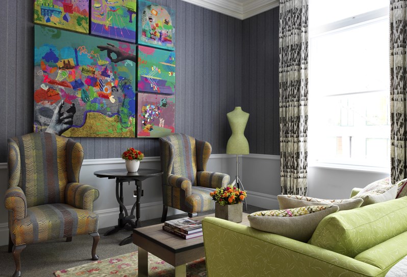 Beautiful living room in one of the bedrooms with sofa and a couple of comfy chairs, showcases a colourful statement art work and the Firmdale signature mannequin